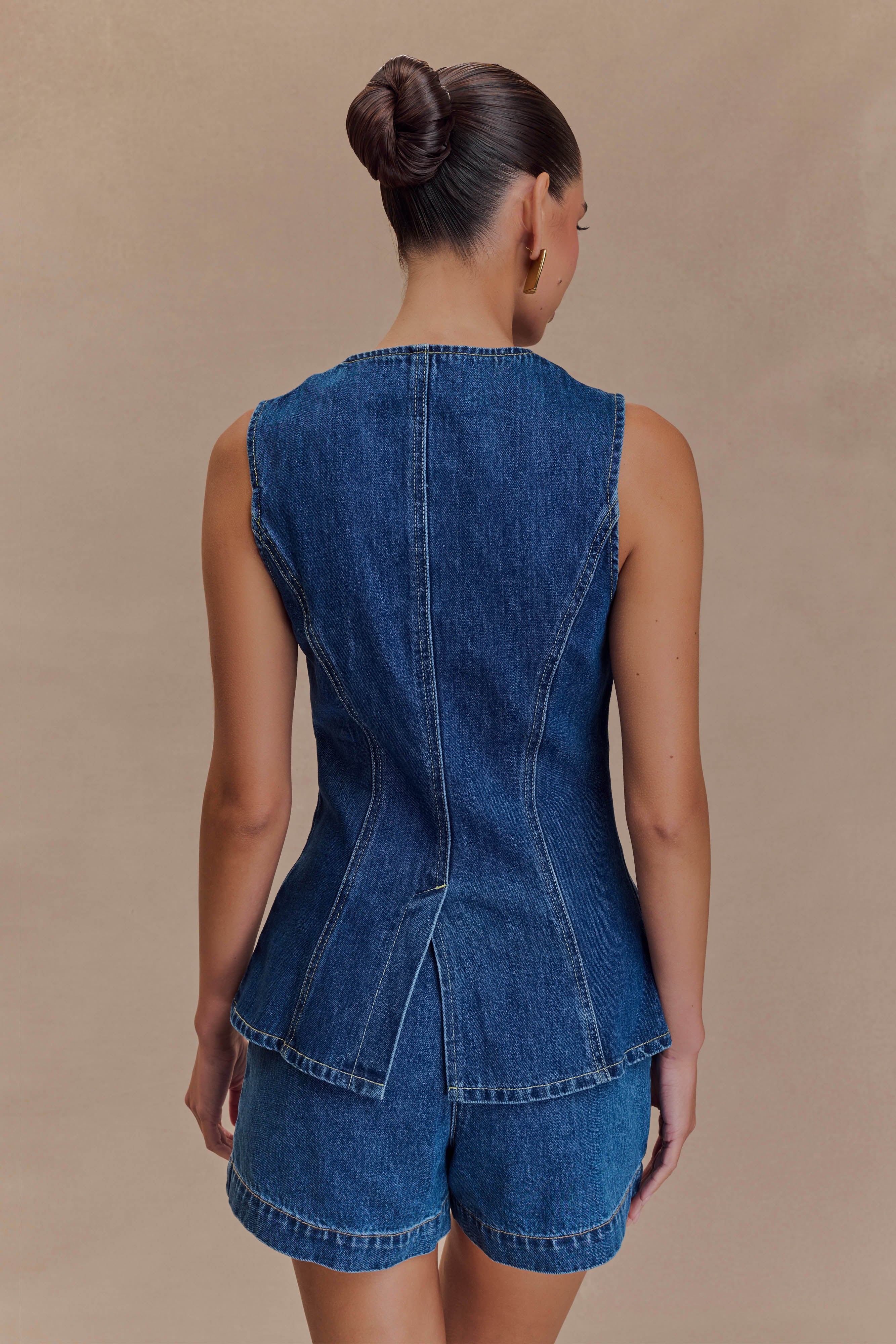 Back view of blue denim sleeveless vest with curved hem and yoke seam