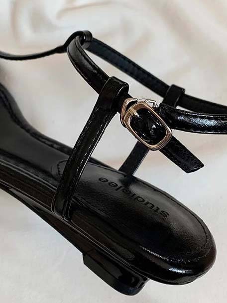 Black faux leather T-strap flat sandal with round buckle ankle strap detail