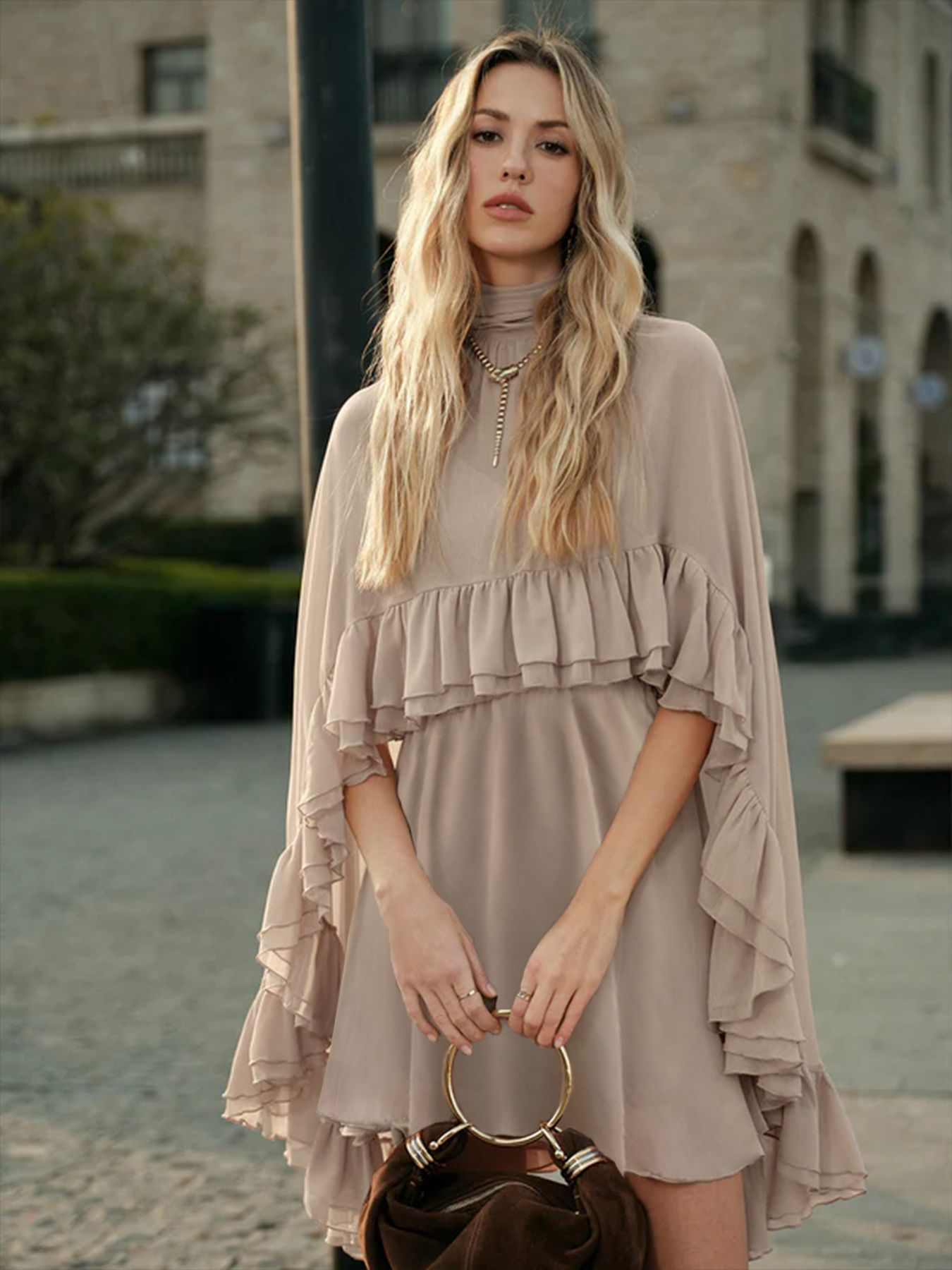 Beige chiffon mini dress with high neck, cape sleeves, and tiered flowy ruffles.