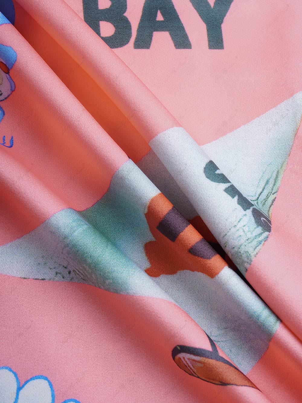 Satin fabric close-up with pink and orange tropical scene print and teal accents