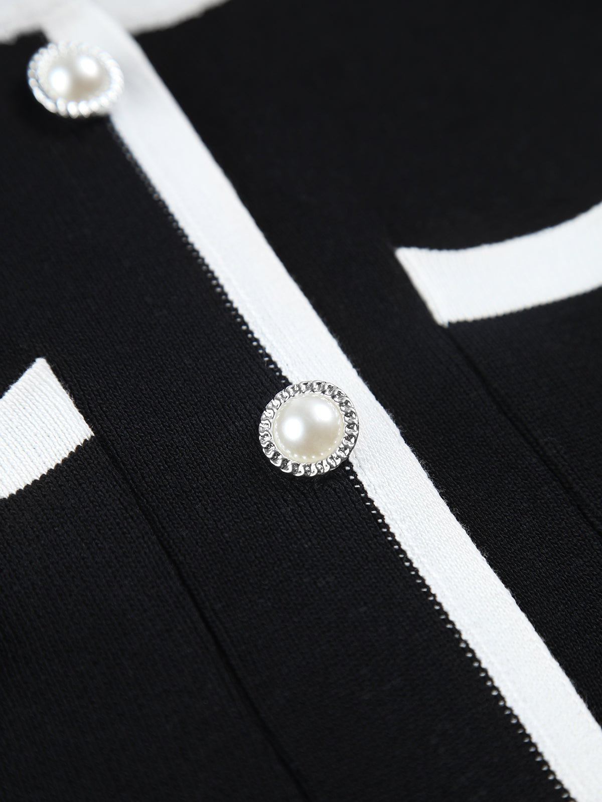 Close-up of black knit dress with white trim and round pearl button detail on front placket