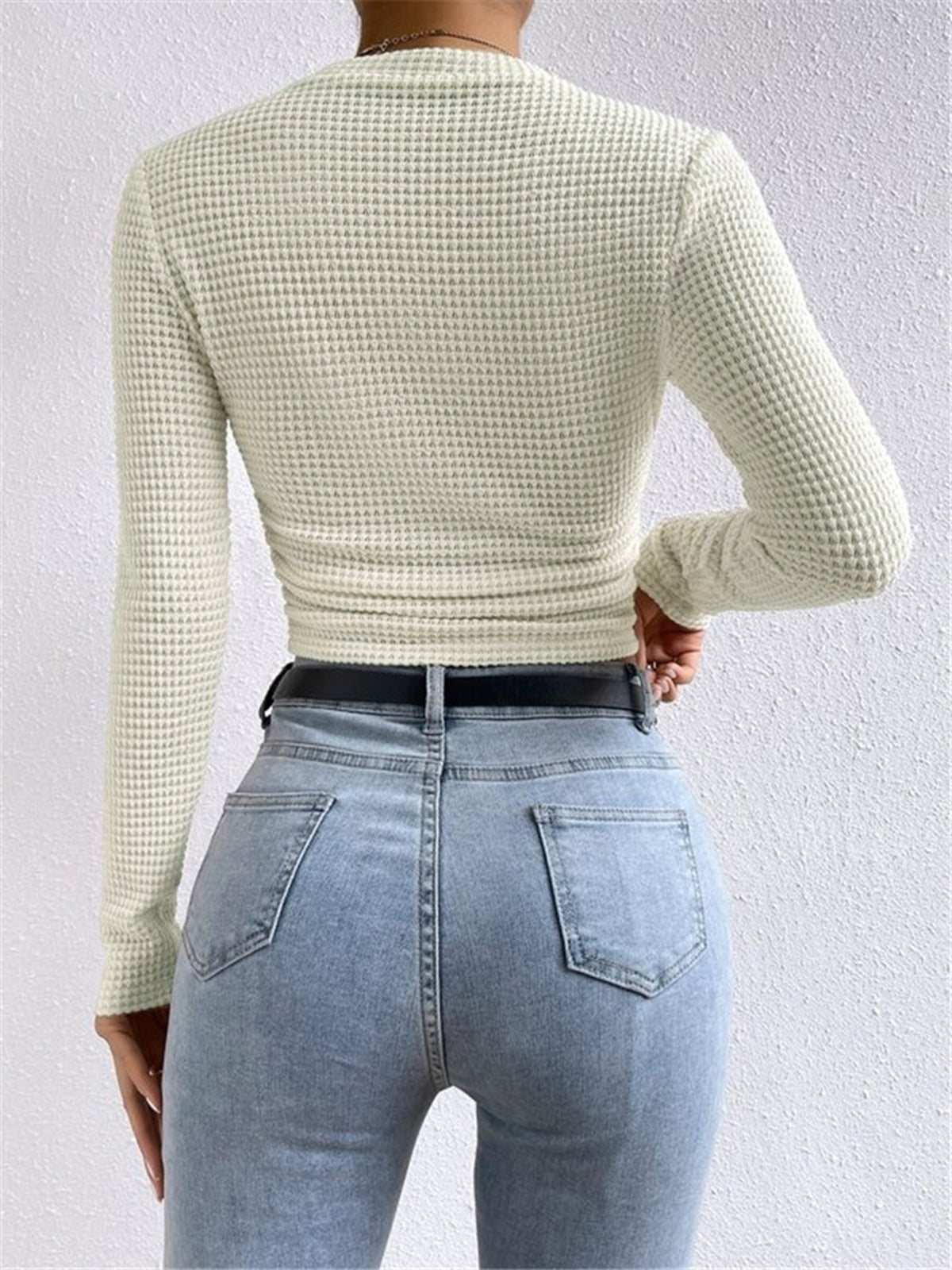 Back view of light cream waffle-knit long-sleeve slim crop top with ruched hem.
