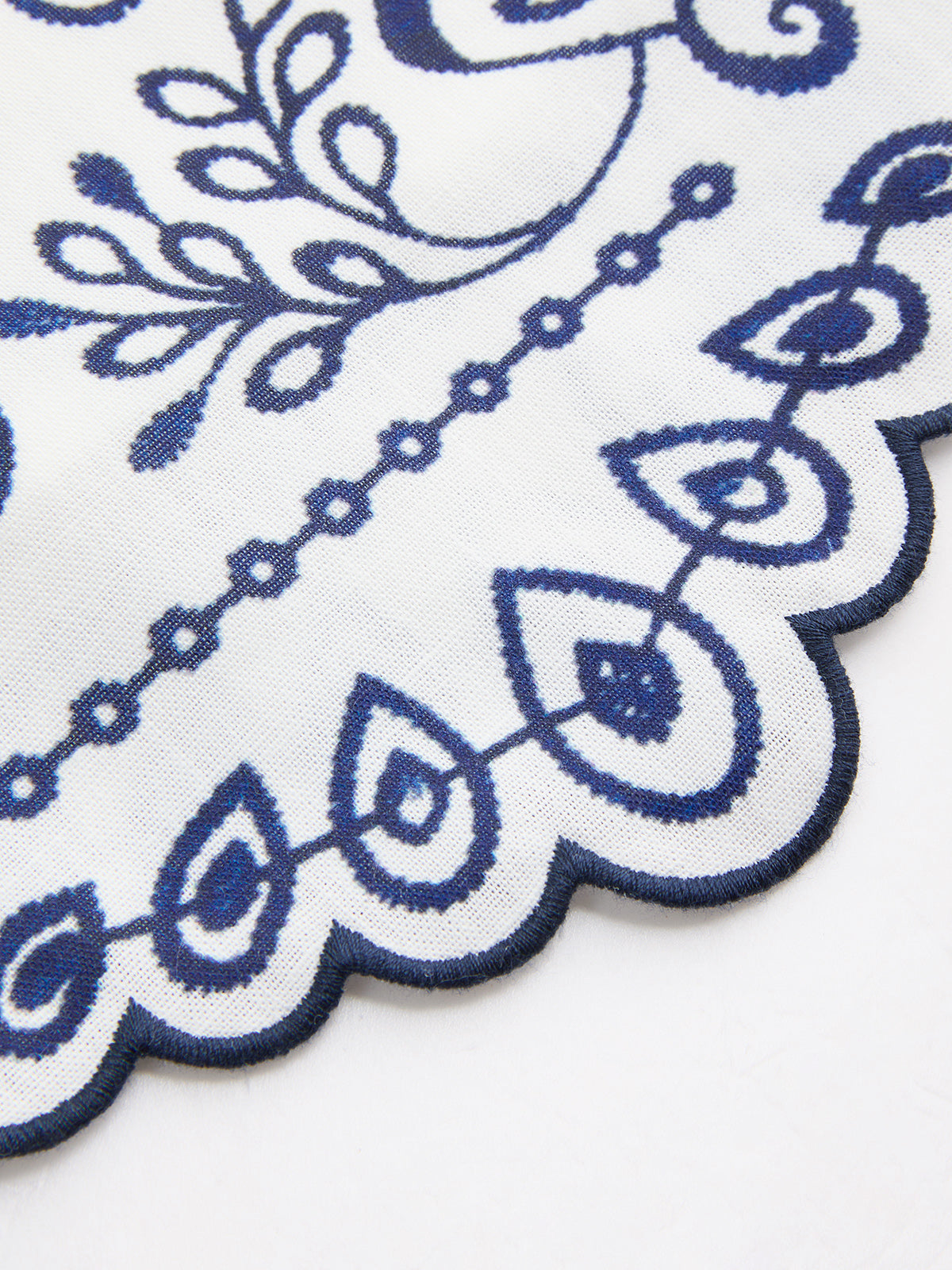 Scalloped hem close-up with blue embroidered trim on white fabric