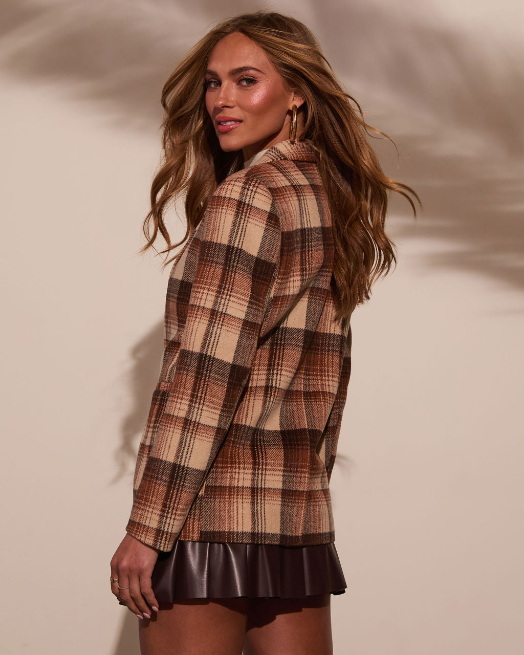 Side view of brown plaid blazer with lapels and patch pockets; leather skirt hem visible