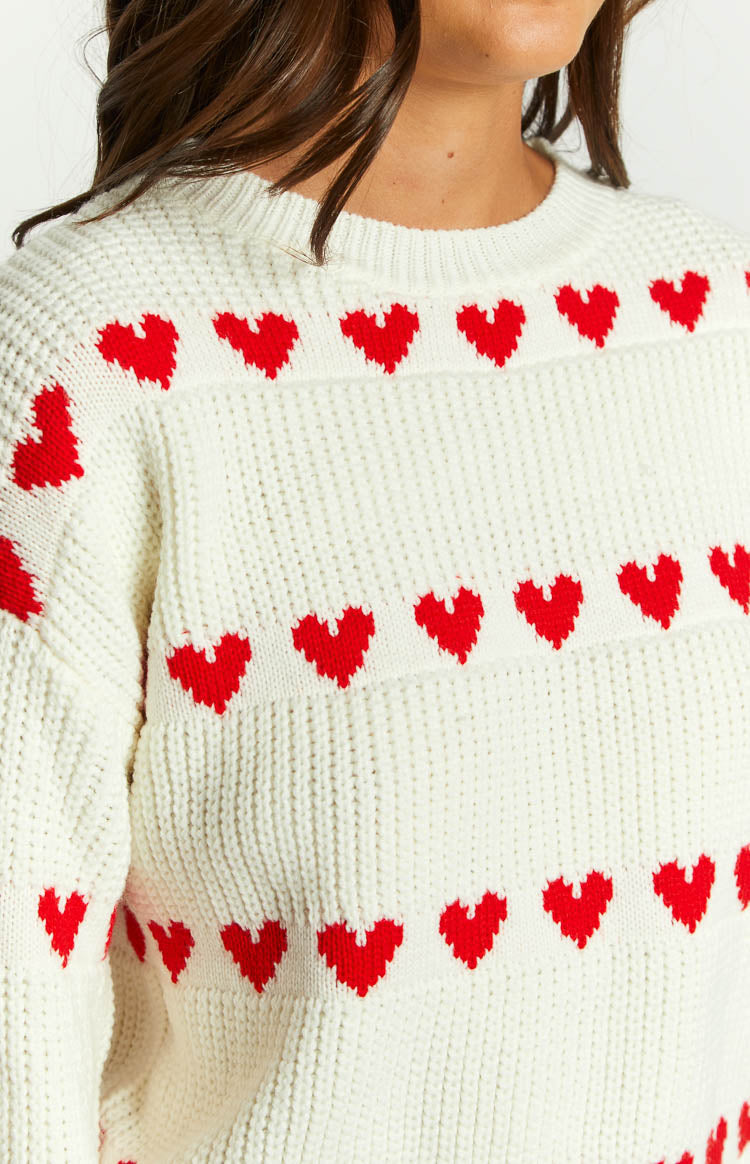 White knit jumper close-up with red heart stripe band across chest