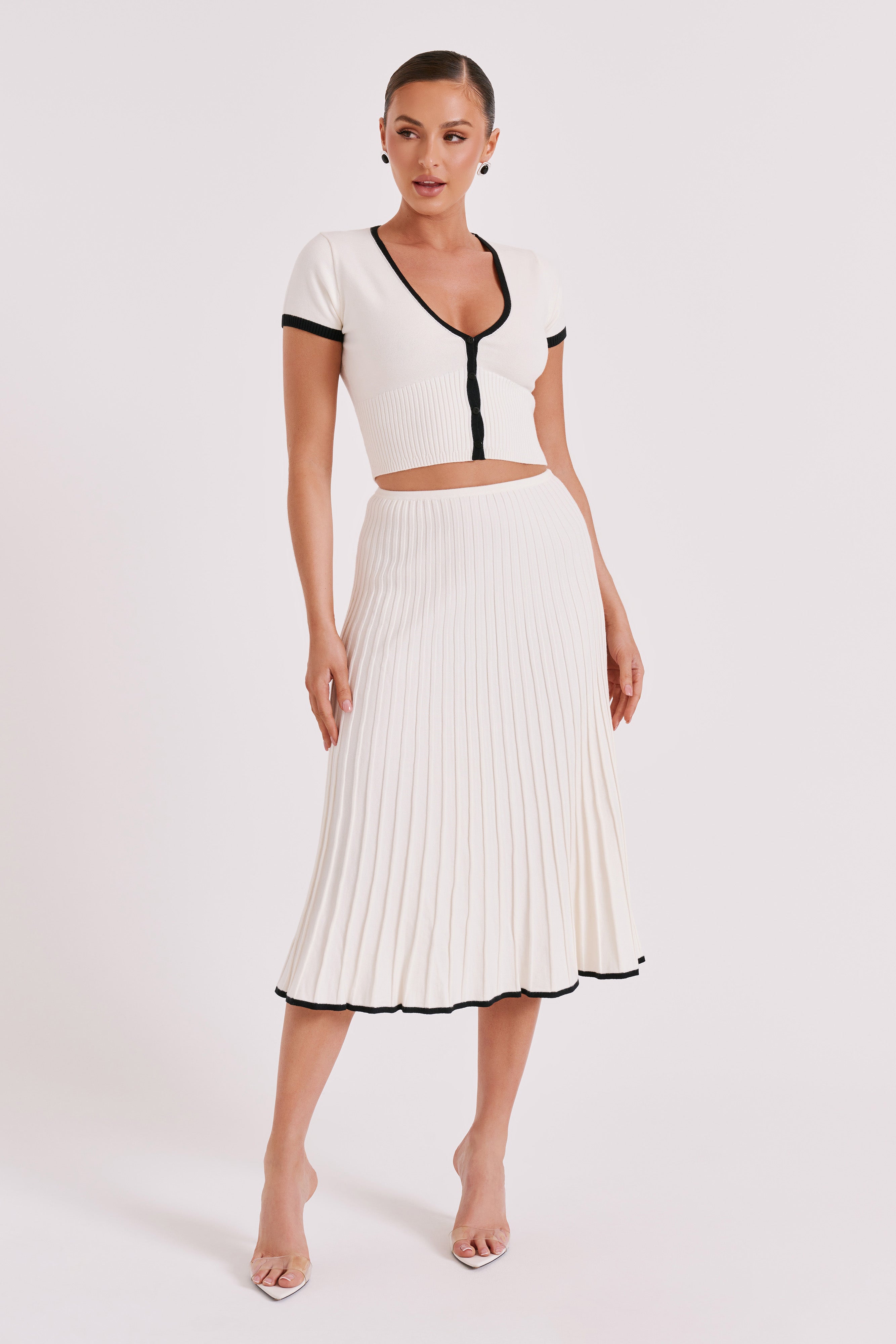 White ribbed crop top with deep V button front and pleated midi skirt, black-trim detail.