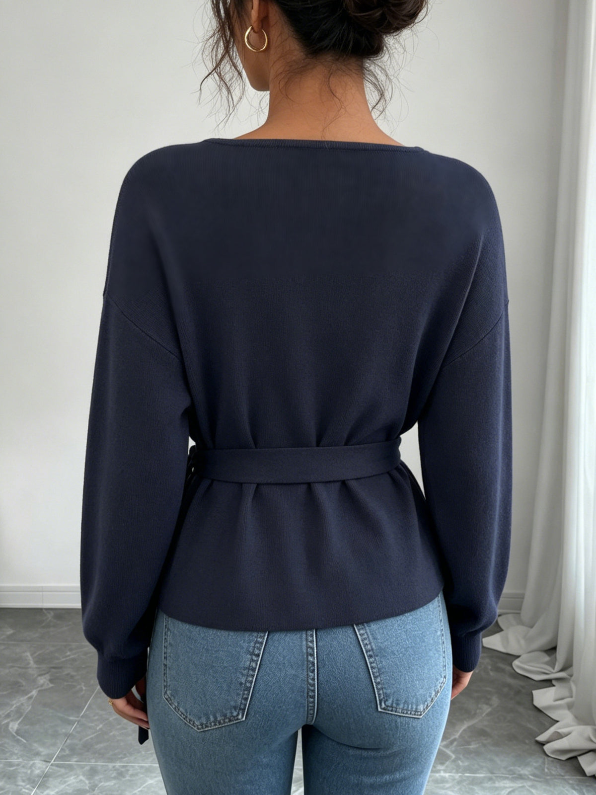 Back view of a women's dark blue knit sweater with a waist tie and loose sleeves