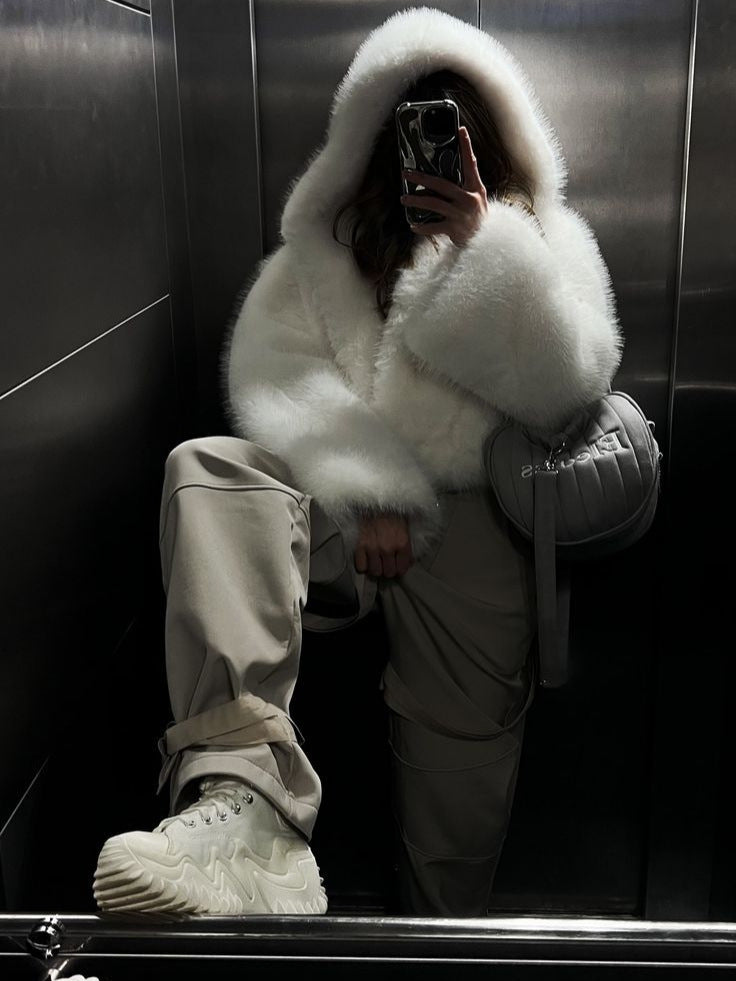 White hooded faux fur coat with plush sleeves, worn with dark pants