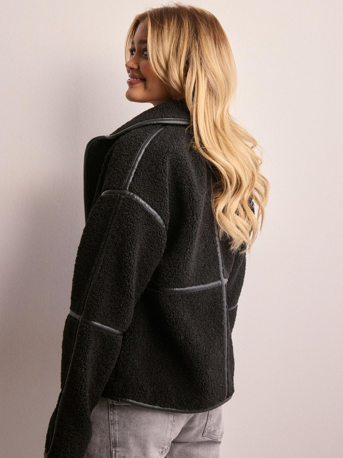 Back and side view of a black fleece jacket with contrast piping and a relaxed fit