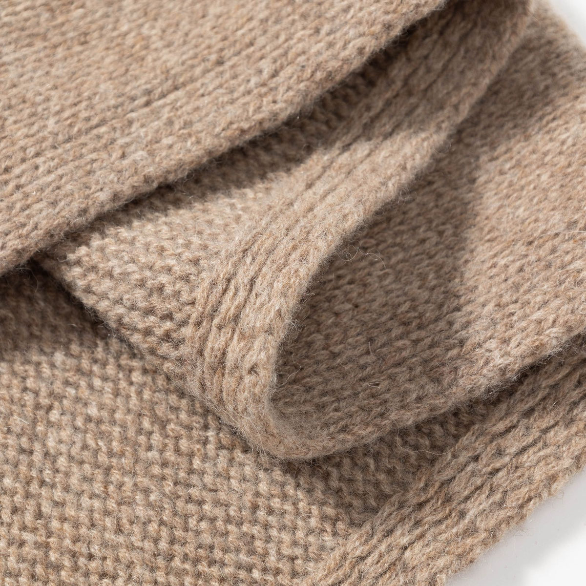 Close-up of beige knitted wool triangle scarf with ribbed seam detail