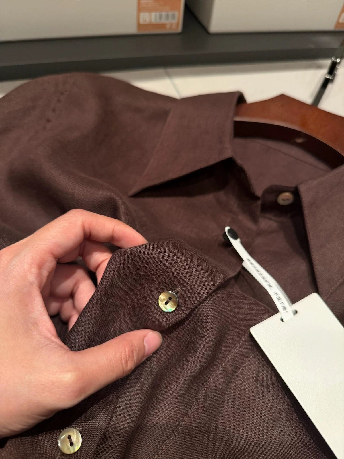 Dark brown linen button-down shirt with chest pocket and brass button placket.