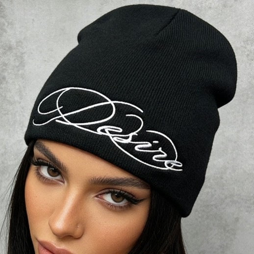 Black knit beanie with white cursive “D” style letter embroidery at front.