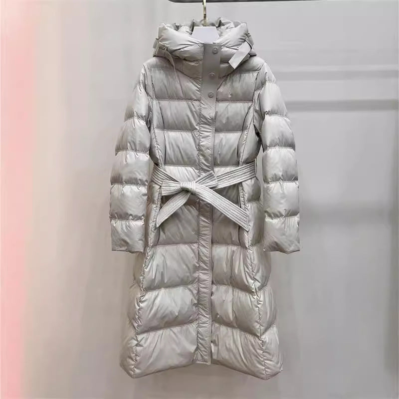 Light gray long puffer coat with belted waist, hooded collar, glossy quilted puffer