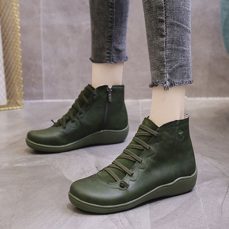 Dark green women's ankle boots with flat soles, lace-up fronts and side zippers, worn on feet.