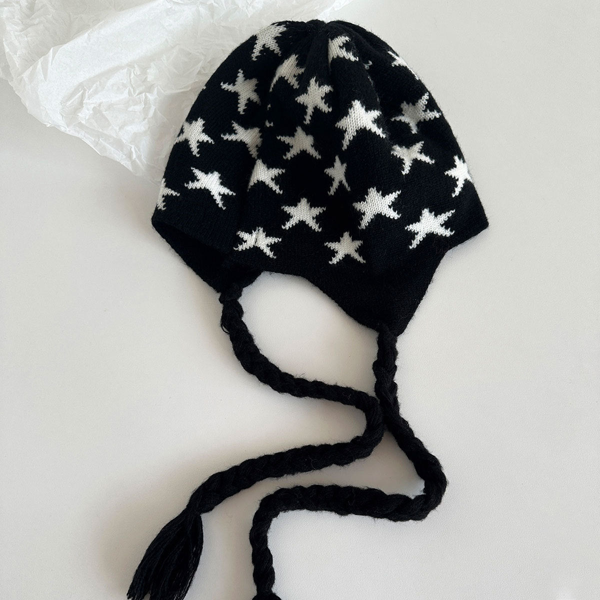 Black knit beanie with white stars and long tie tassels, flat lay
