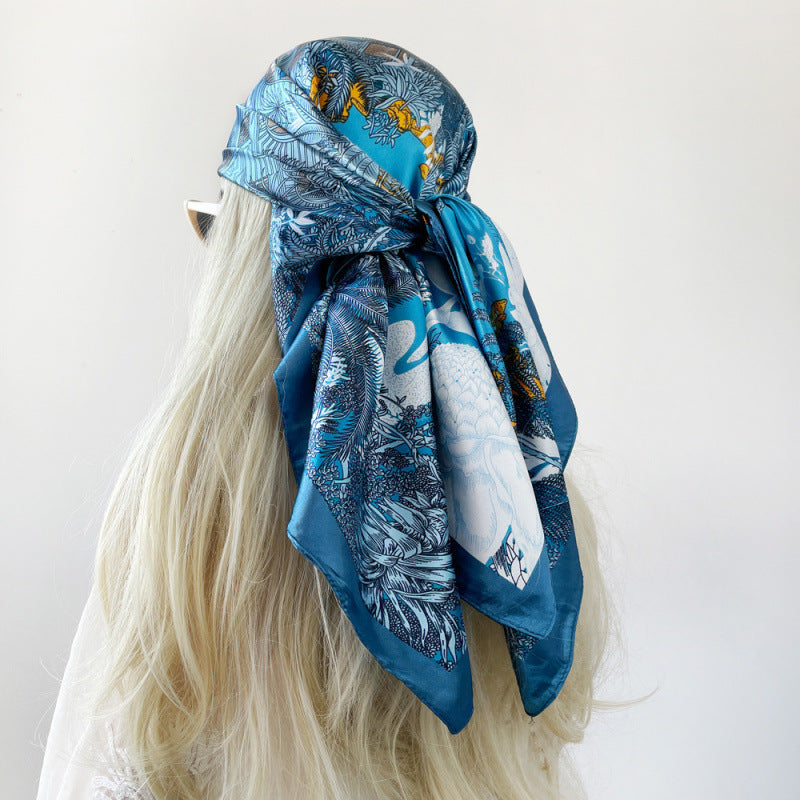 Blue silk square scarf with tropical leaf and bird print, draped with rolled edge.