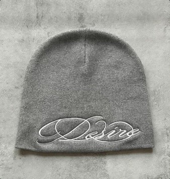 Grey knit beanie with white cursive “D” style letter embroidery on front.