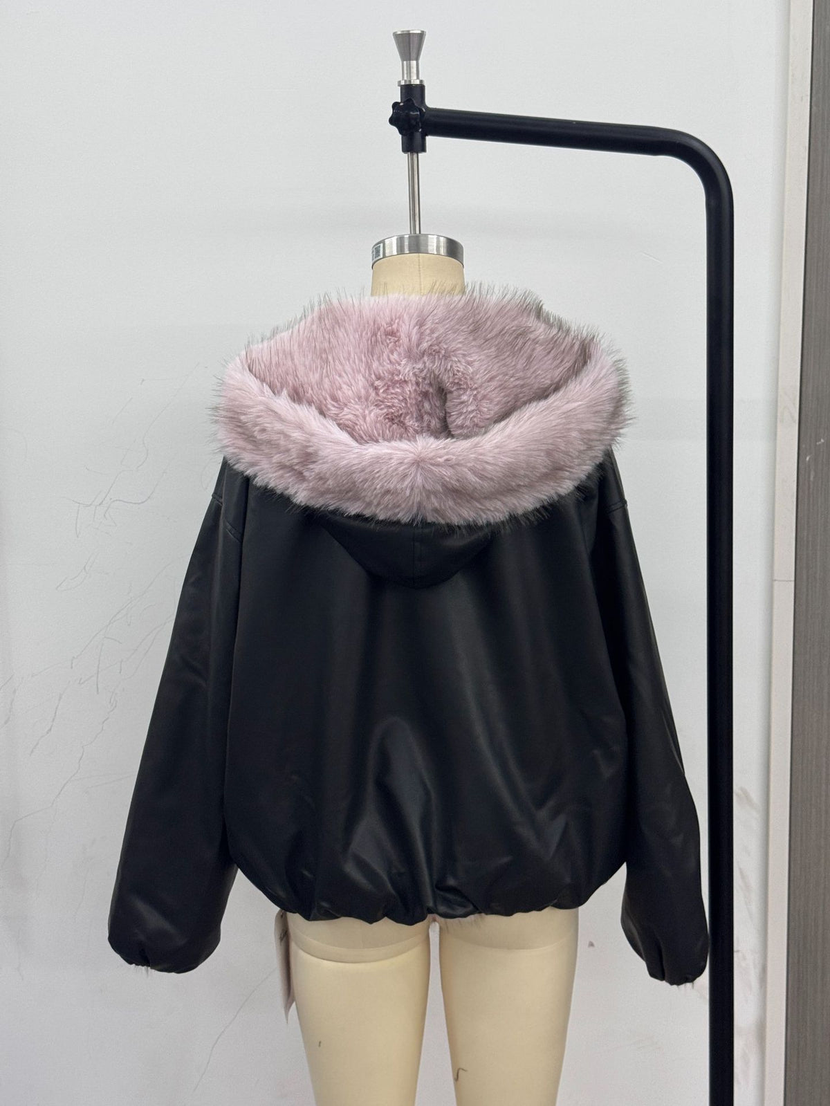 Women’s black leather jacket with light pink faux fur lined hood, back view on hanger