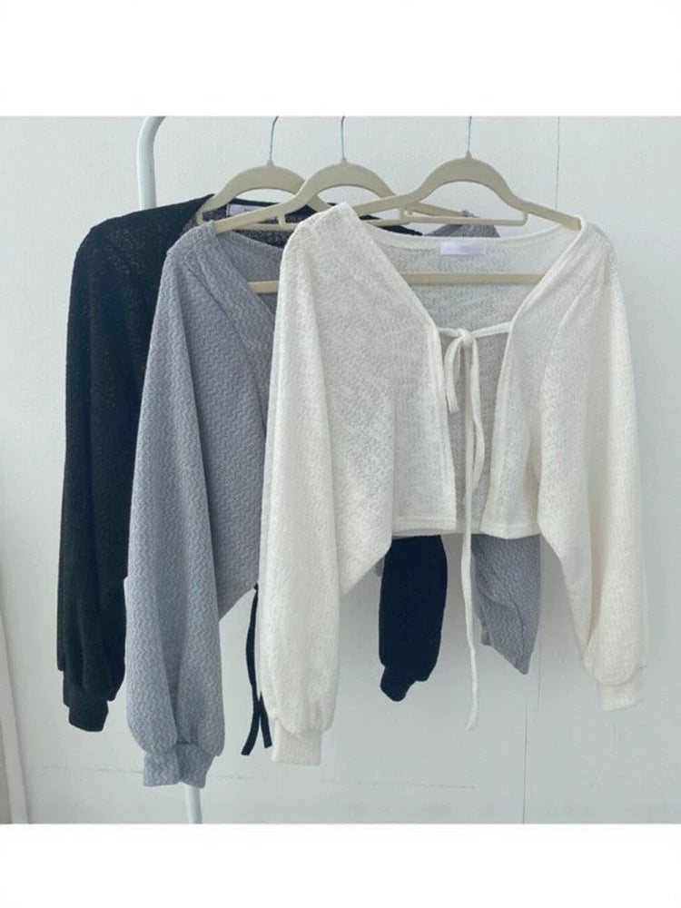 Set of three cropped tie-front open-knit cardigans in white, gray, and black on hangers