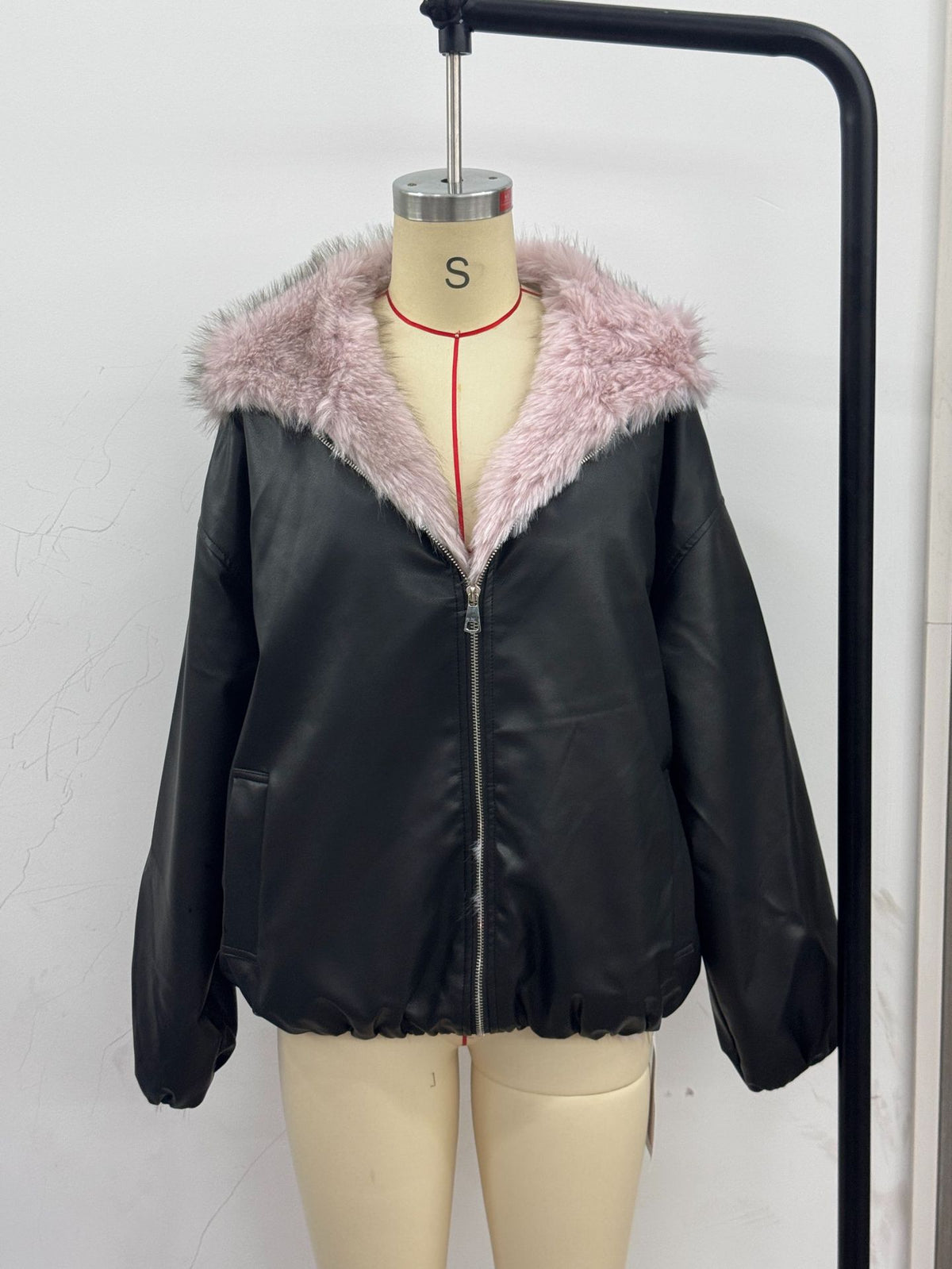 Women’s black leather jacket with light pink faux fur hood and zip front on hanger