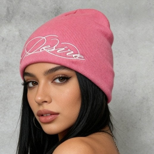 Pink knit beanie with white cursive “D” style letter embroidery on front.