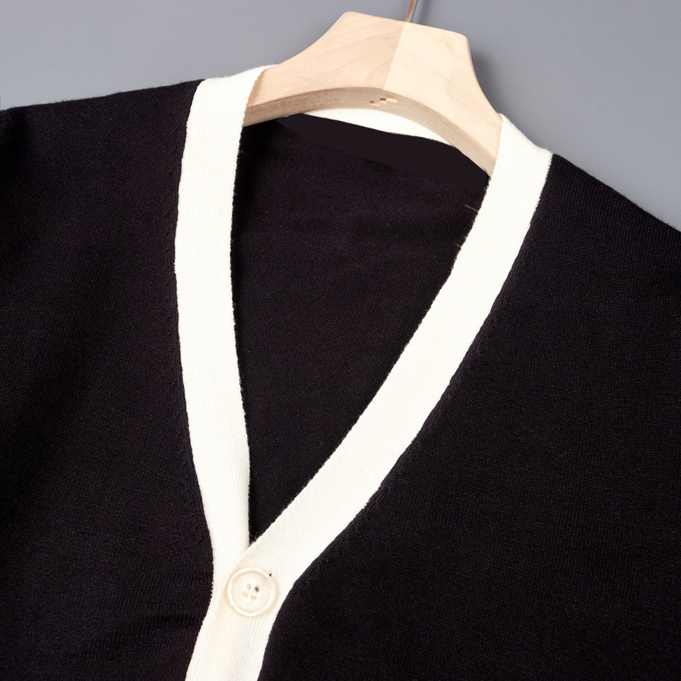 Close-up of black V-neck knit cardigan with off-white trim and round button placket