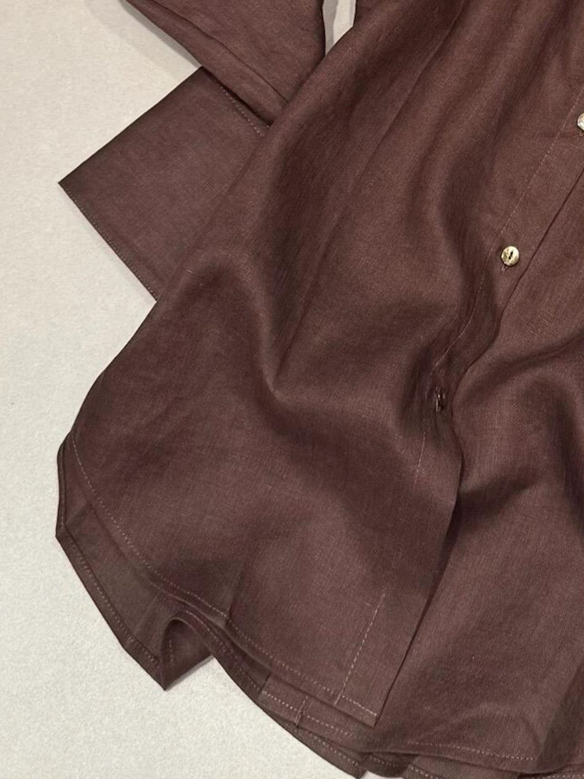Dark brown linen button-down shirt, shirttail hem and chest pocket detail.