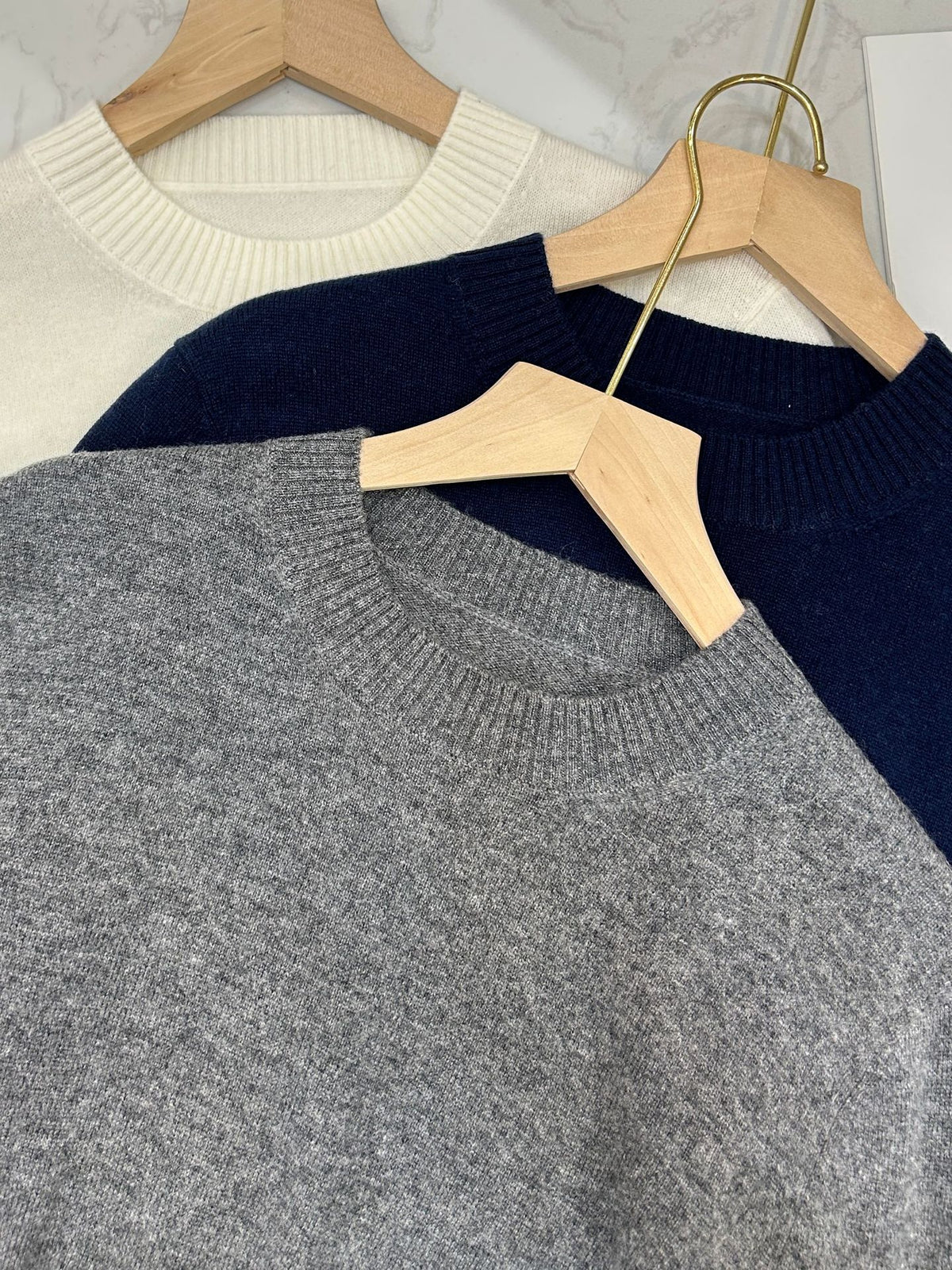 Gray crewneck knit sweater with ribbed neckline and long sleeves, close-up on hangers