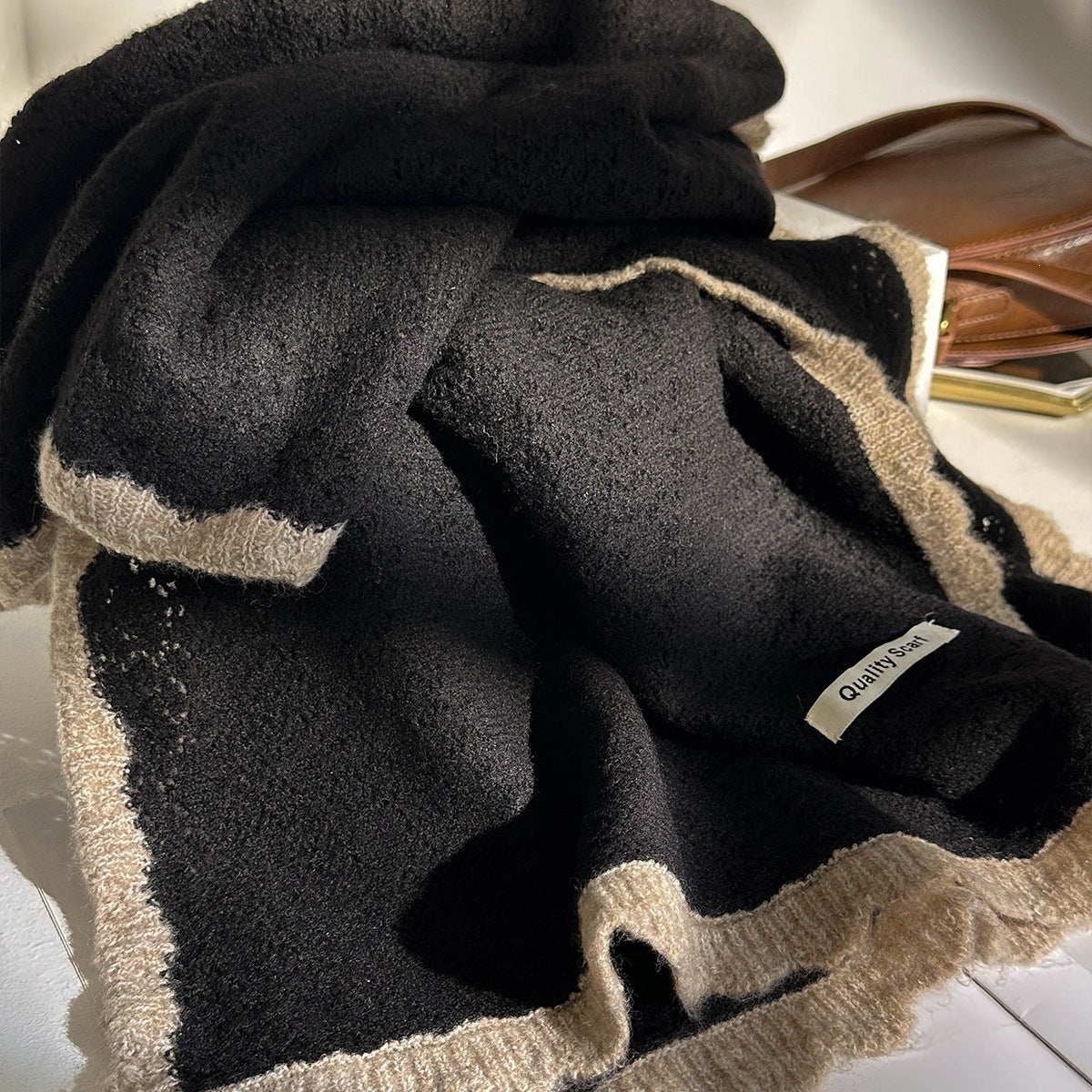 Charcoal black lace-knit wool scarf with tan border and label, neatly folded.