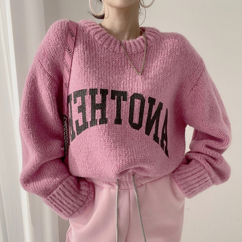 Pink chunky knit crewneck sweater with black slogan graphic over white straps