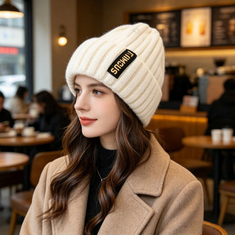 Cream-white ribbed knit beanie with folded cuff and branded patch on the side
