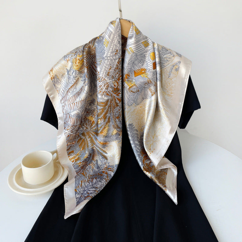 Beige silk square scarf with gold and orange tropical print, draped over shoulders.