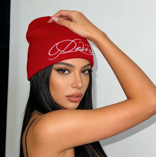 Red knit beanie with white cursive “D” style letter embroidery, slouch fit.