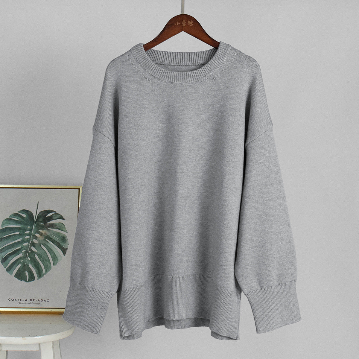 Light grey round-neck knit sweater on a hanger with ribbed collar and cuffs