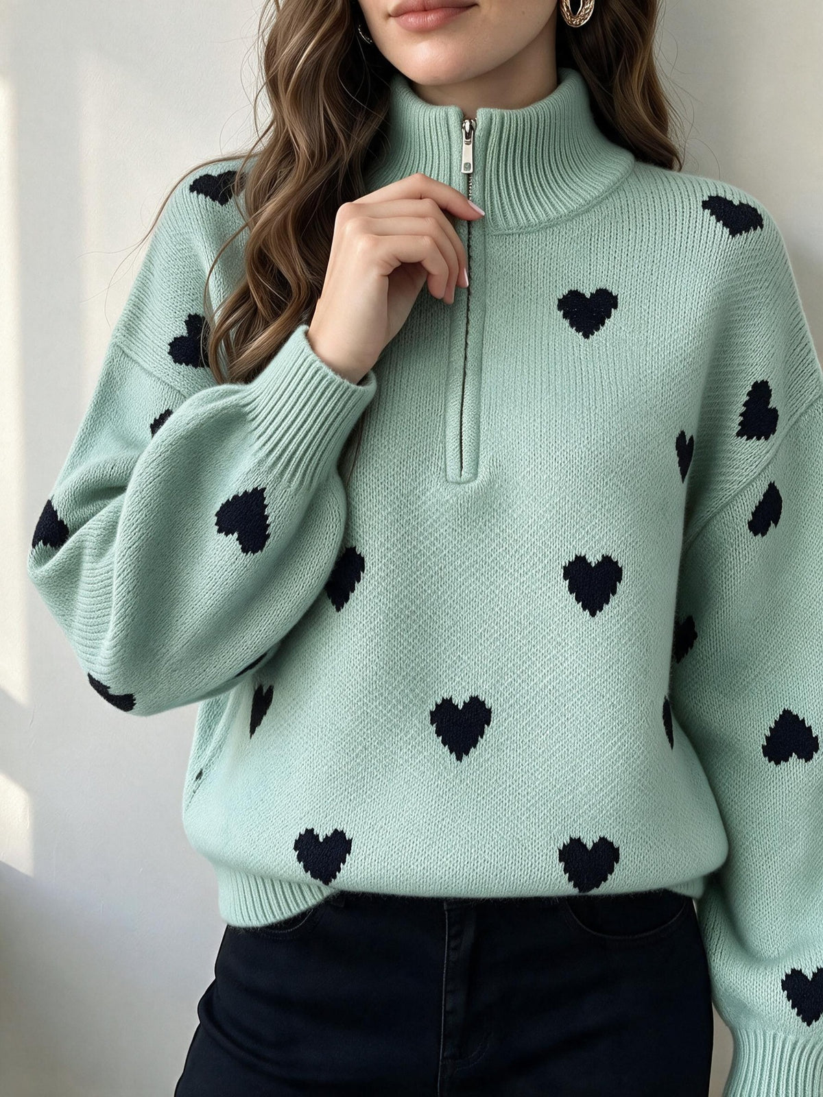 Light green knit sweater with black hearts, ribbed high neck and front zipper.