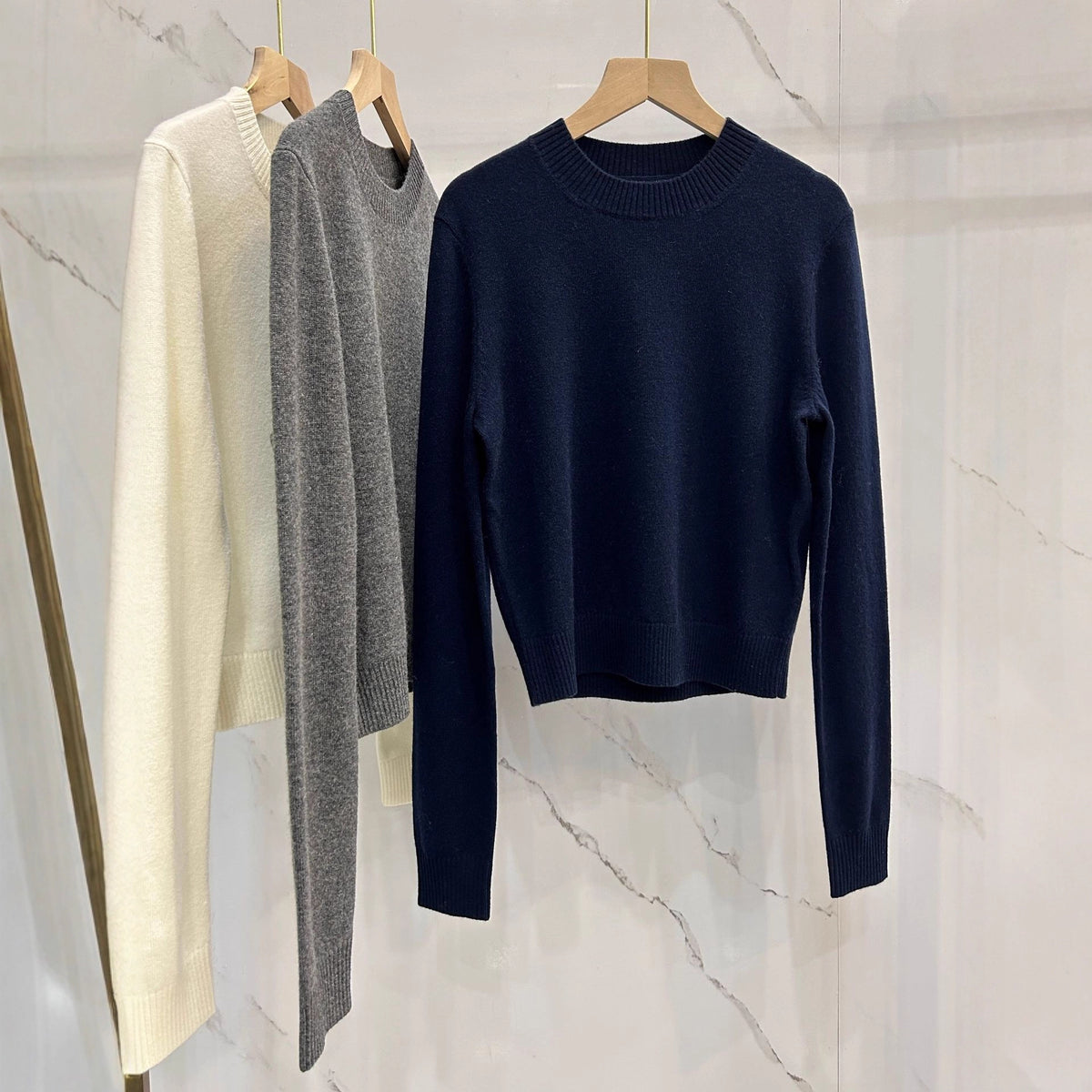 Crewneck knit sweater in off-white, gray, and navy, long sleeves on hangers