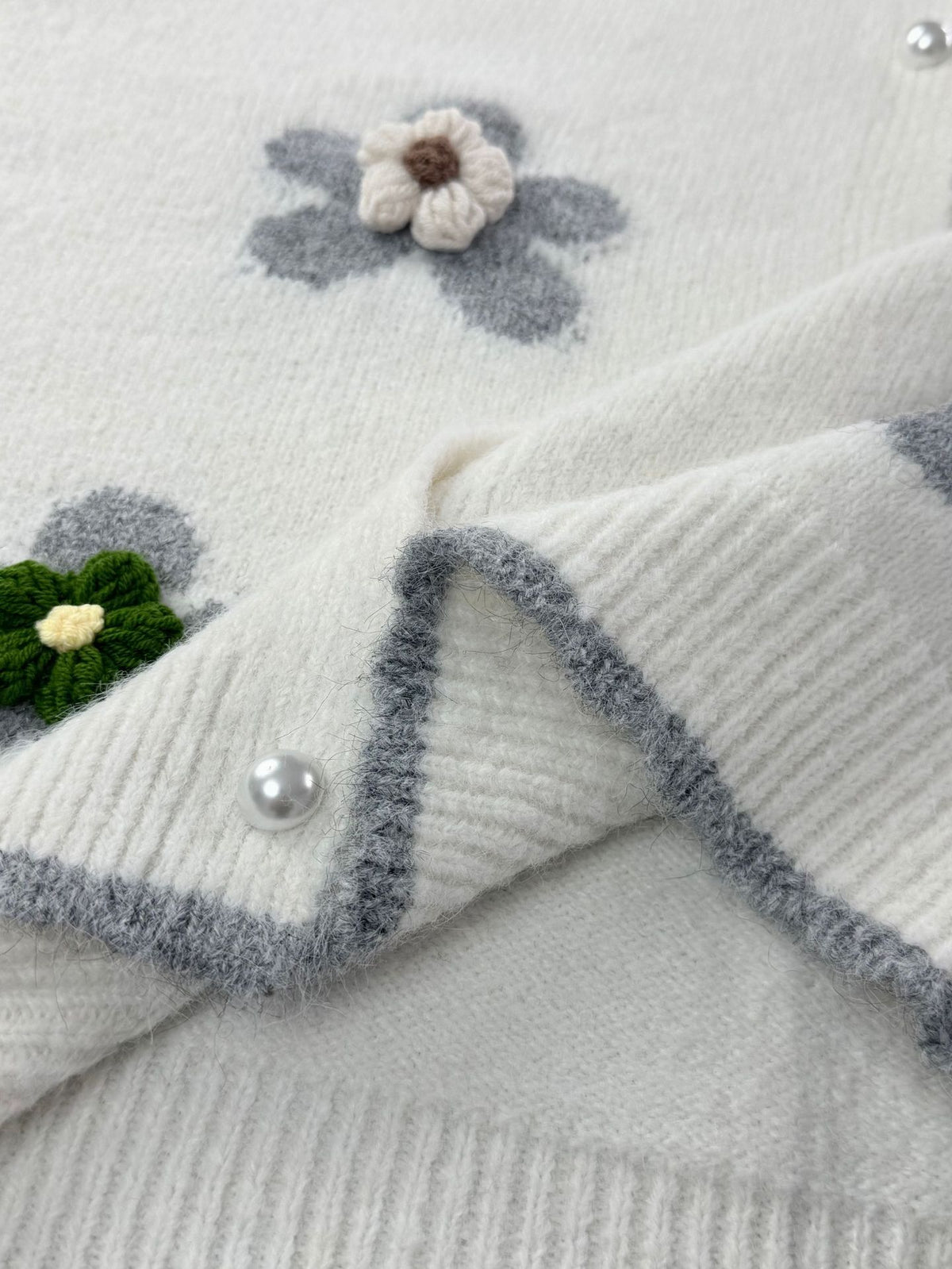 Close-up of women’s cream knit cardigan with textured trim, floral applique, pearl button