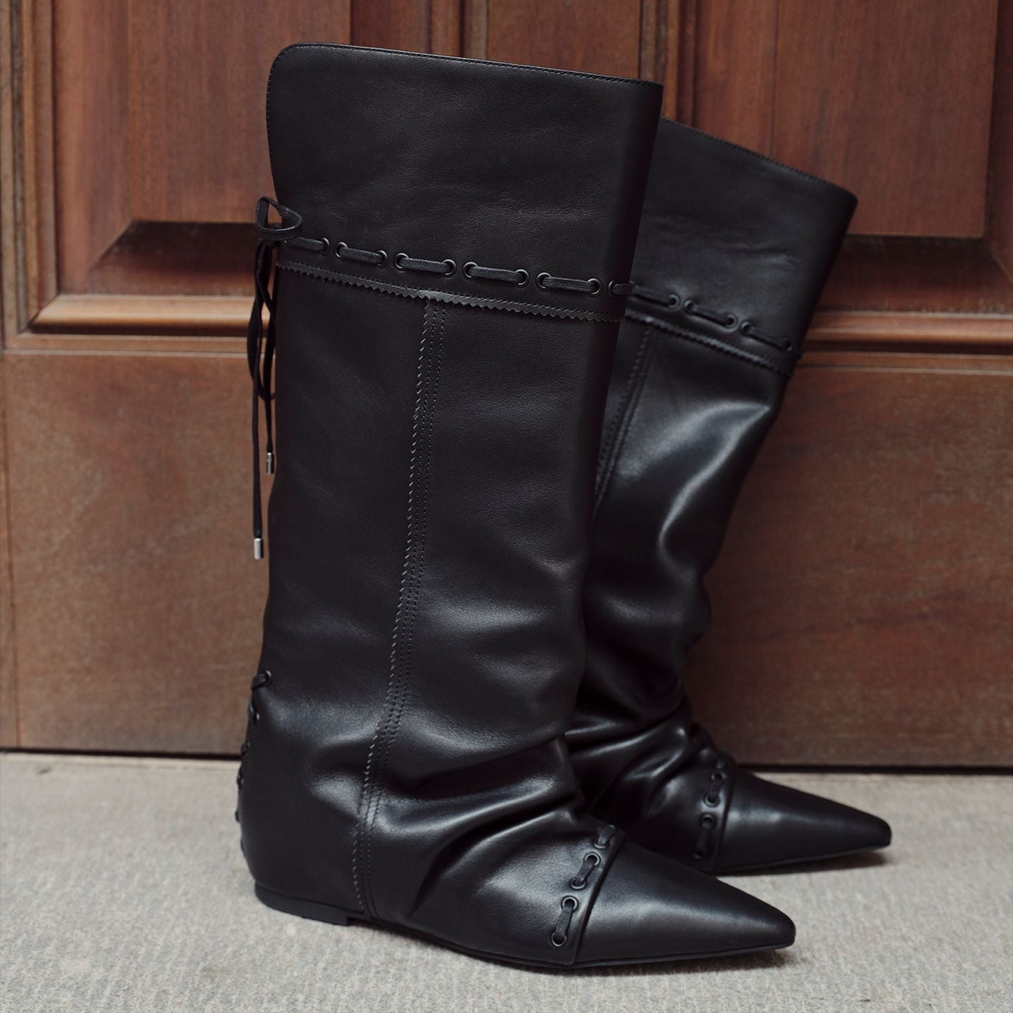 Black knee-high slouch boots, pointed toe, side strap with metal eyelets