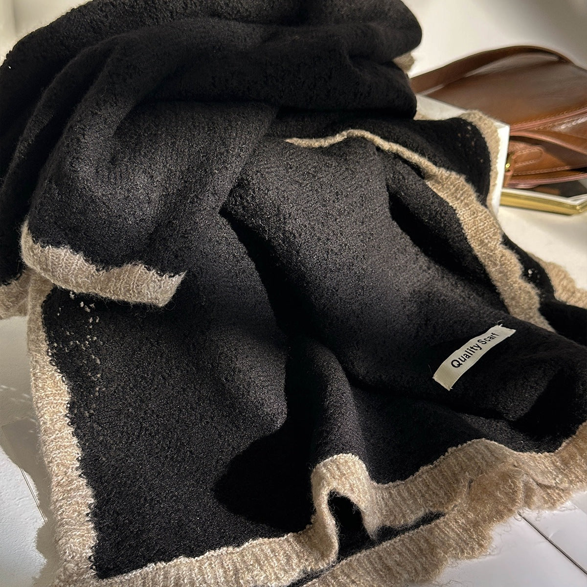 Black lace-knit wool scarf with tan border and fringed edge, folded with label.