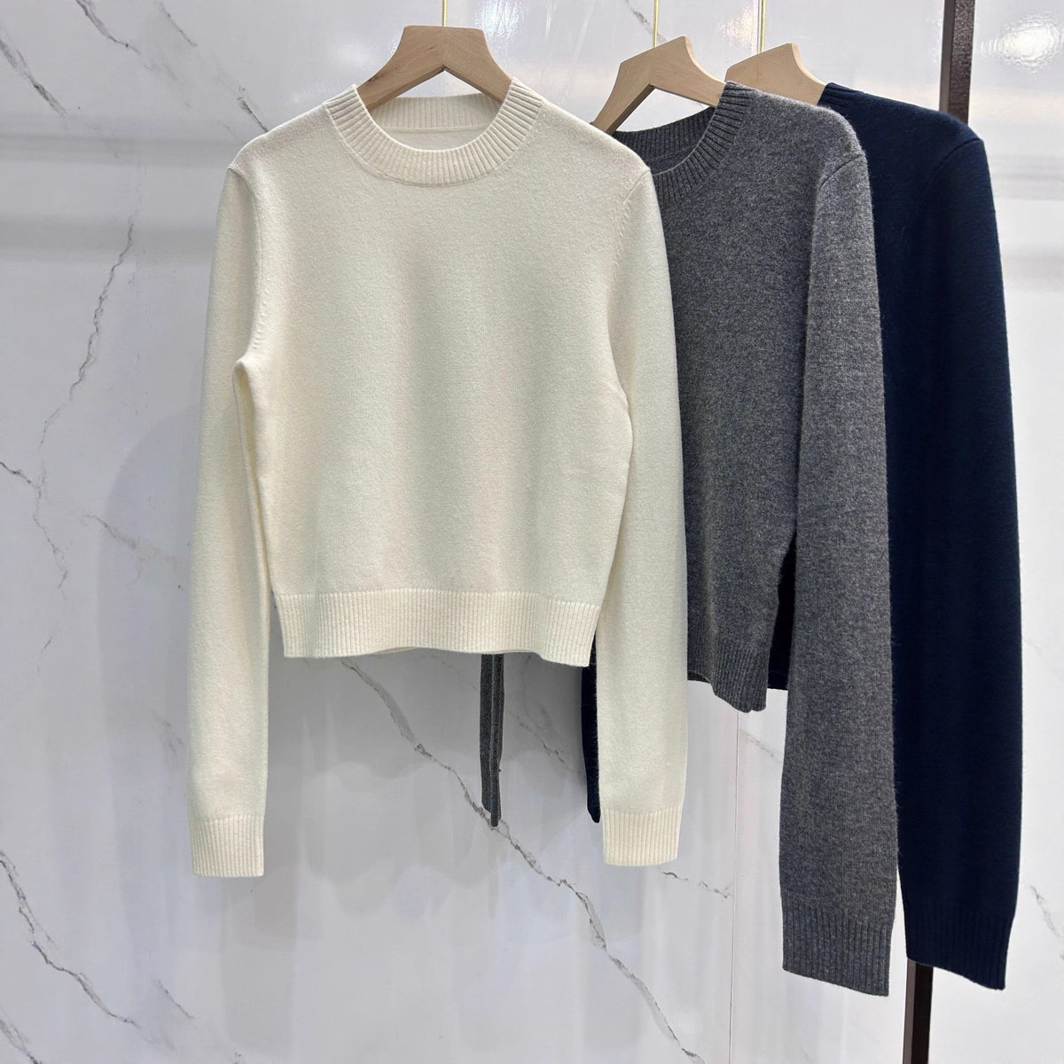 Off-white crewneck knit sweater with ribbed cuffs, with gray and navy options on hangers