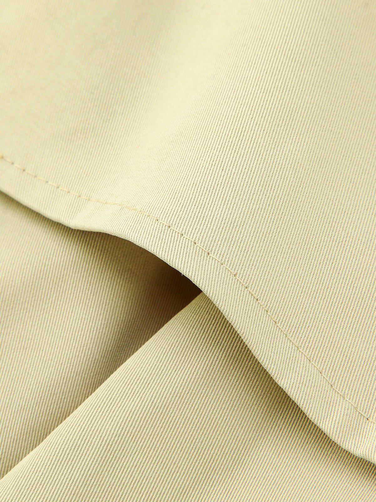 Close-up of light fabric texture and stitched curved hem on a short trench coat