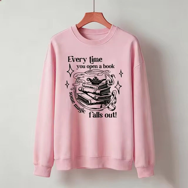 Pink crewneck sweatshirt with open-book magic graphic and starry text, long sleeves.