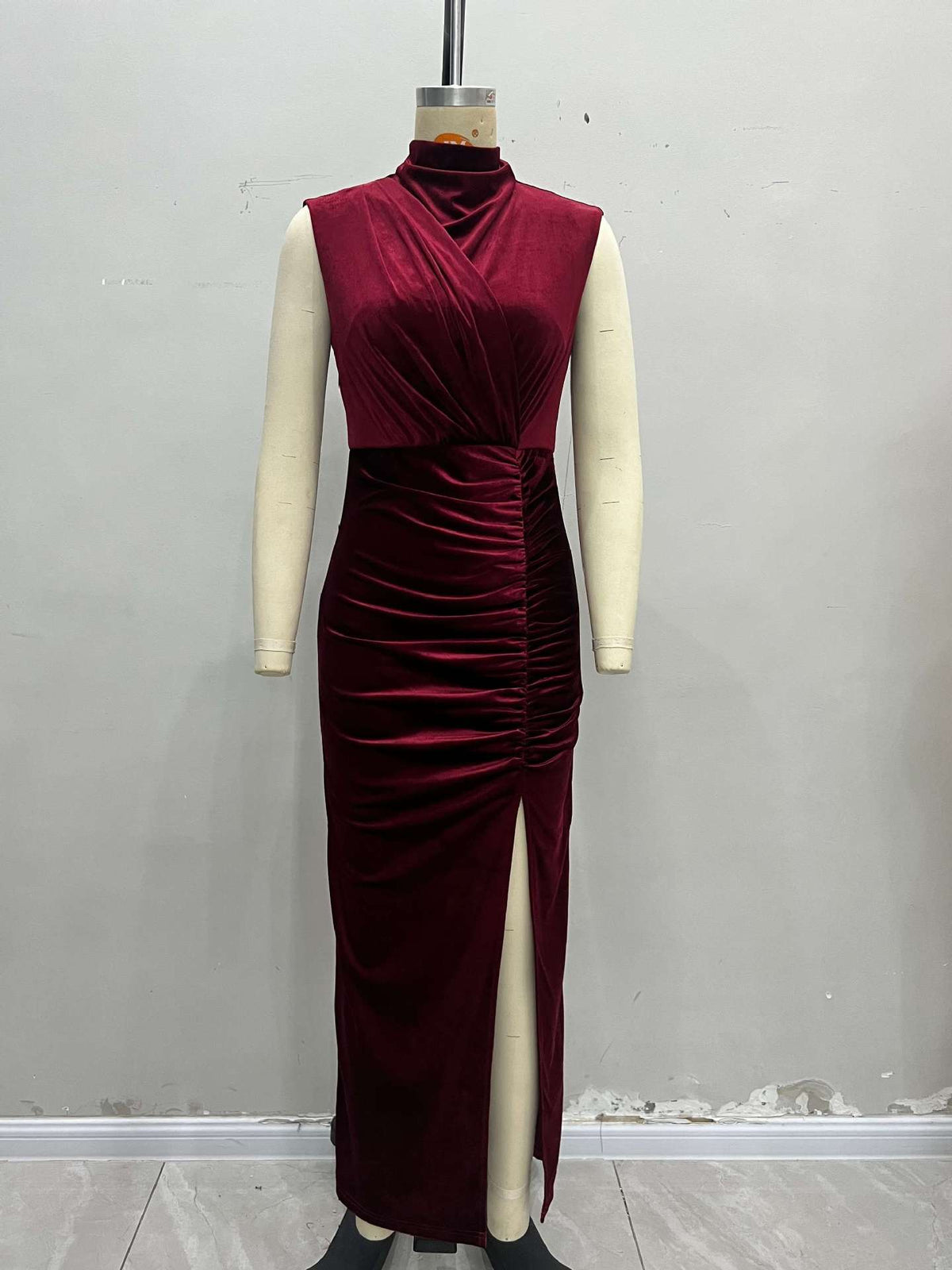 Burgundy velvet sleeveless evening dress on mannequin, stand collar, ruched back, slit.