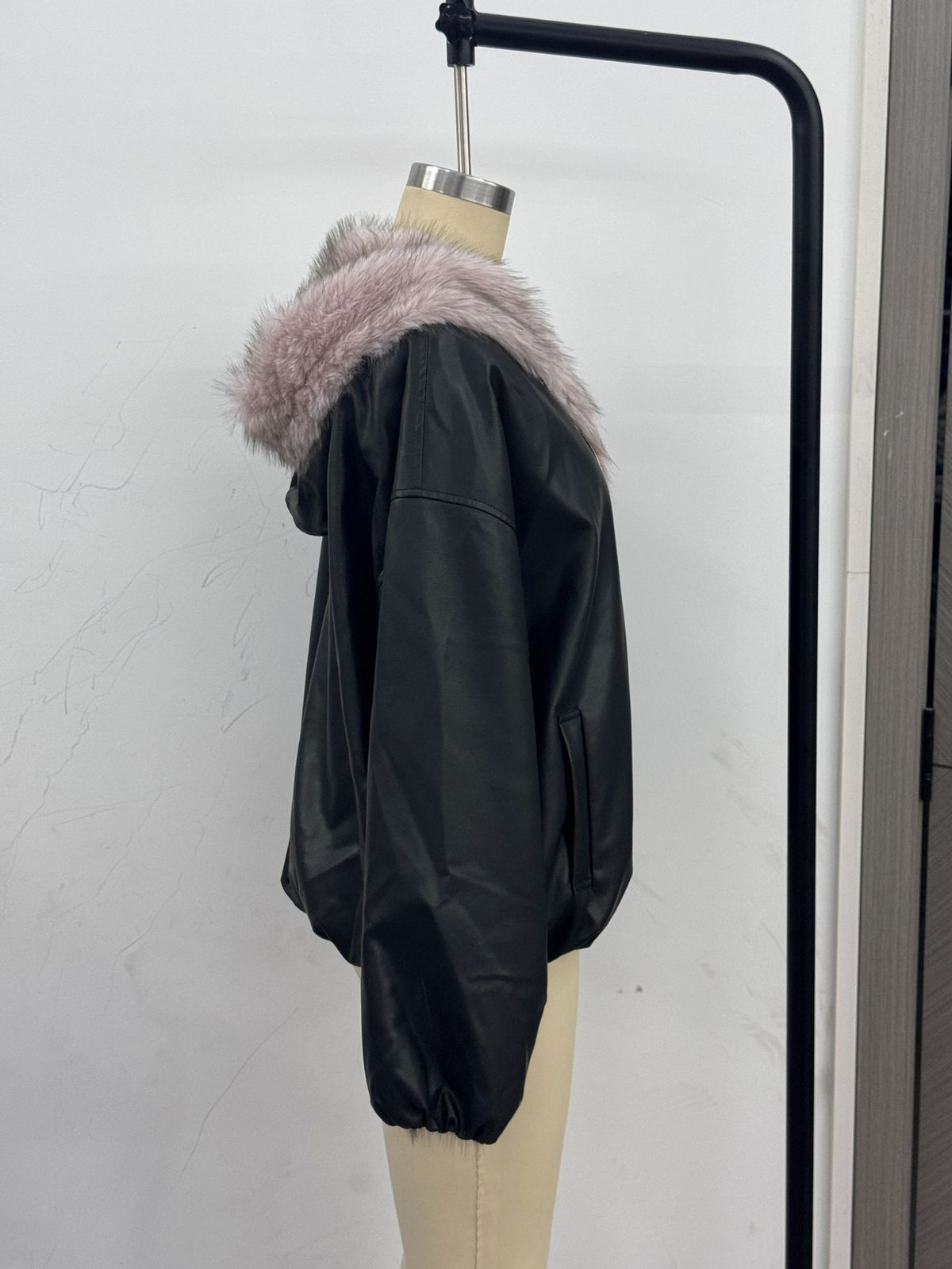 Women’s black hooded leather jacket with light pink faux fur trim, back side view on hanger