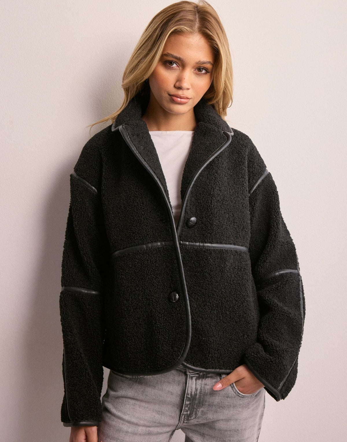 Front view of a black fleece cardigan jacket with a high lapel collar and contrast piping