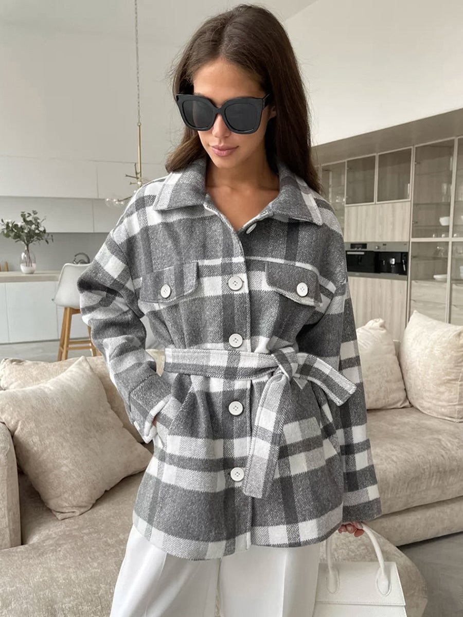Mid-length gray and white plaid wool coat with lapels, buttoned chest pockets, and tie belt