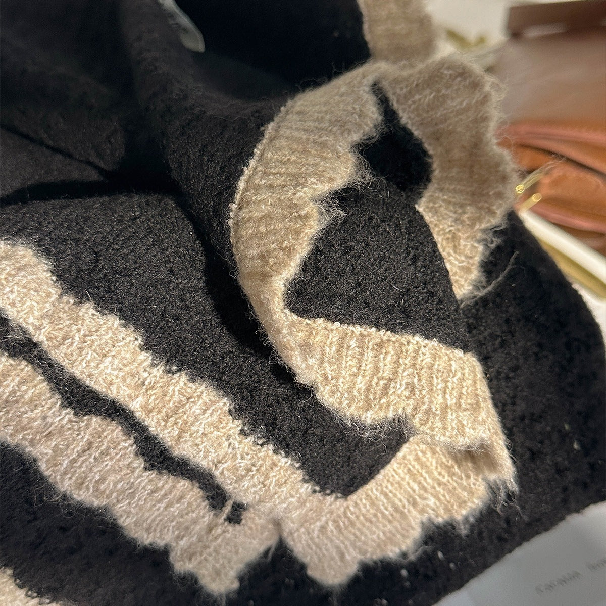 Black-and-beige patterned knit scarf with fringed trim, close-up texture detail.