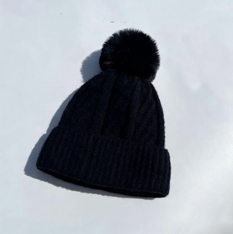 Black cable-knit winter hat with ribbed cuff and fluffy pom-pom
