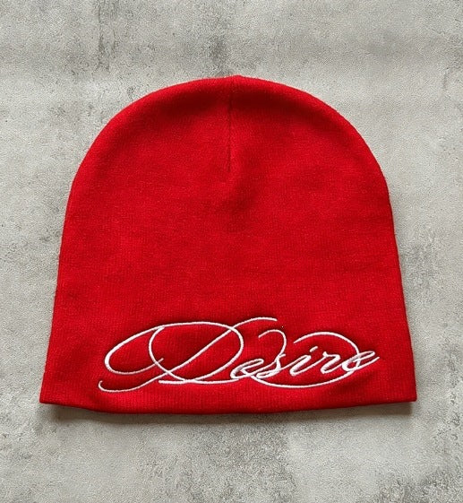 Red knit beanie with white cursive “D” style letter embroidery, flat front.