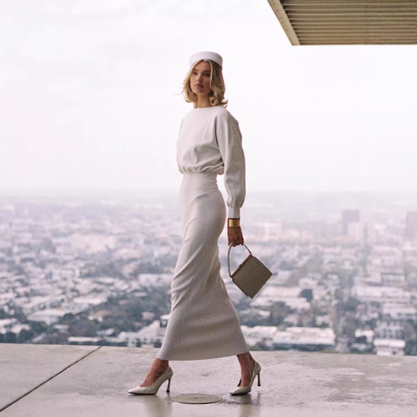 White midi knit dress with cinched waist and long lantern-style sleeves, walking view